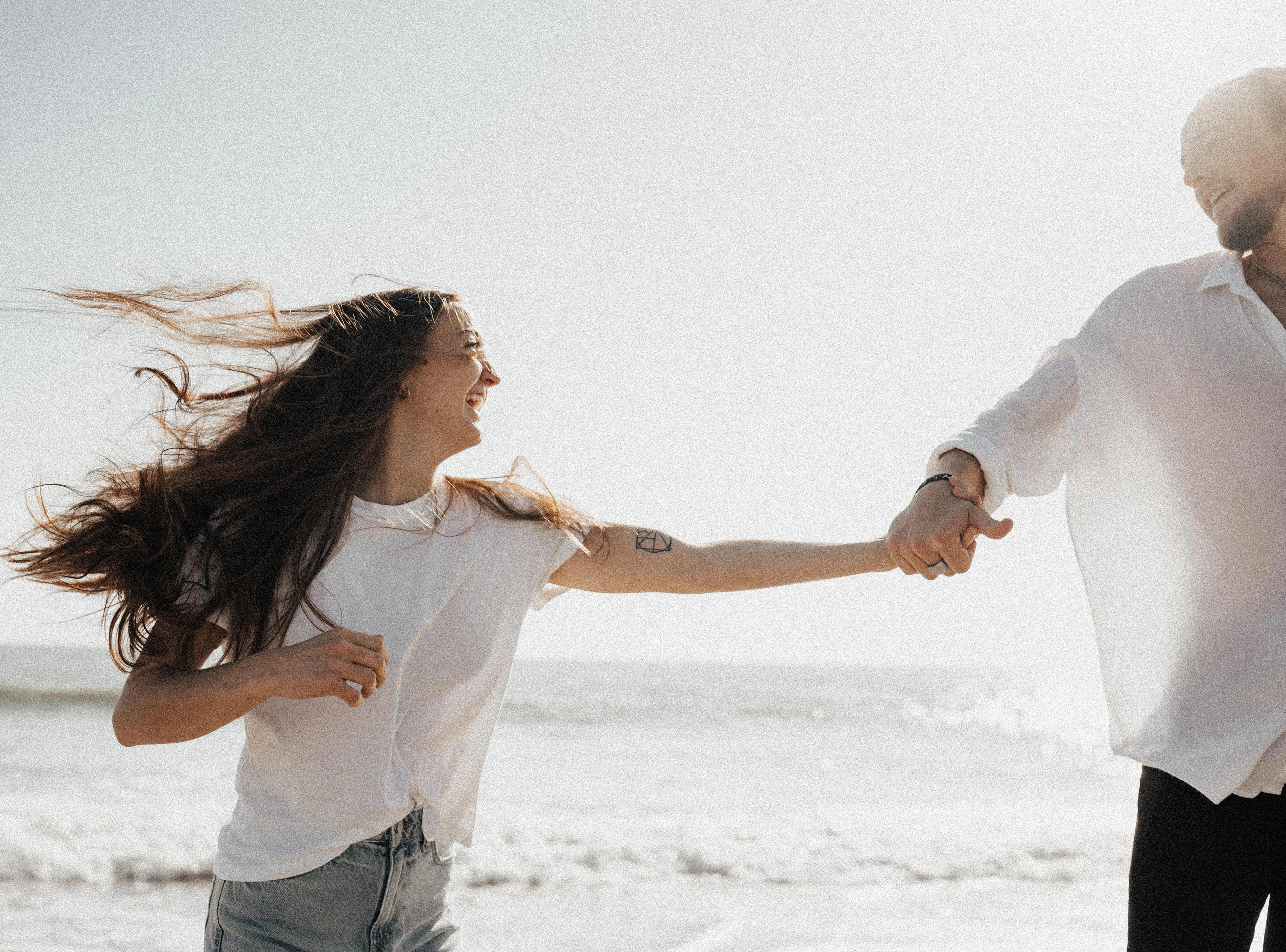 A couple laughing together as they walk hand in hand along the shoreline