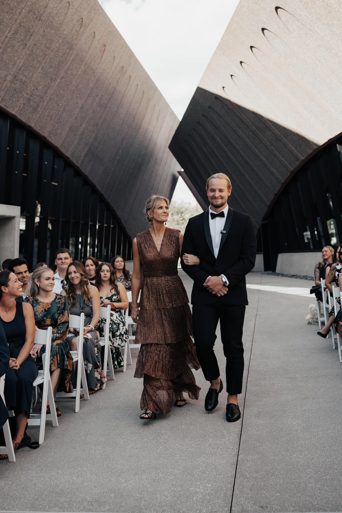 A groom walking down the aisle with guests seated at an outdoor ceremony