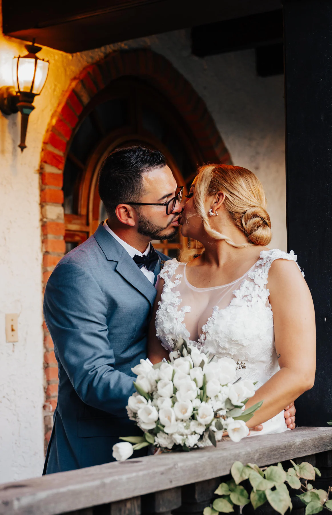 A bride and groom kiss beneath a brick arch at Hacienda Siesta Alegre in Rio Grande, the bride holding a bouquet of white tulips