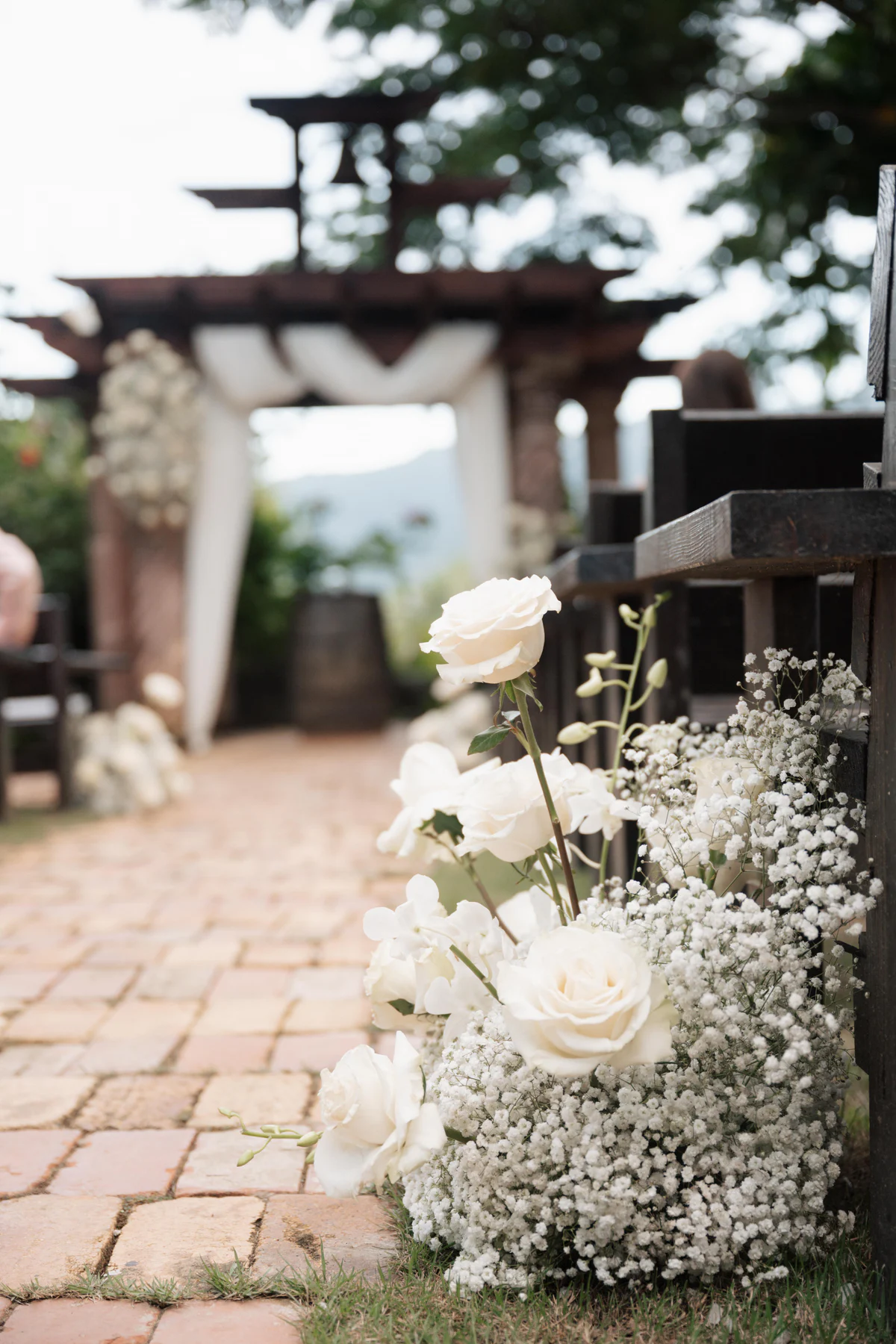 White roses lining the brick ceremony aisle at Hacienda Siesta Alegre, with the pergola behind
