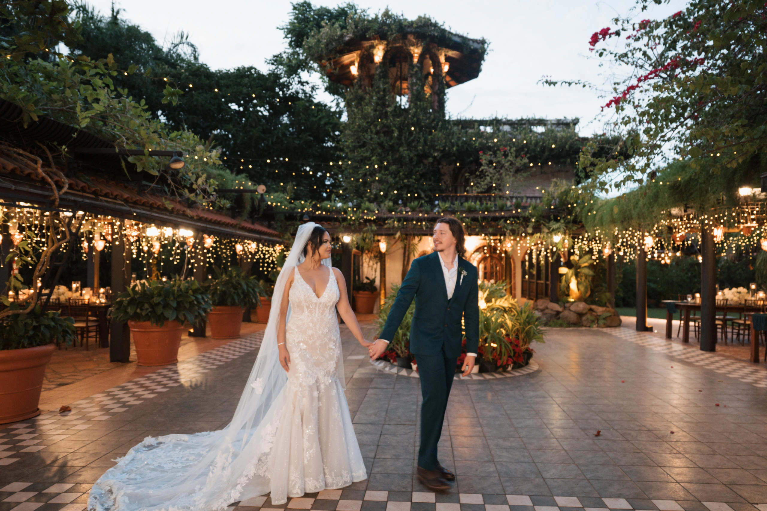 Abigail and Cody walking hand in hand through the string-lit courtyard at their Hacienda Siesta Alegre wedding in Rio Grande, Puerto Rico