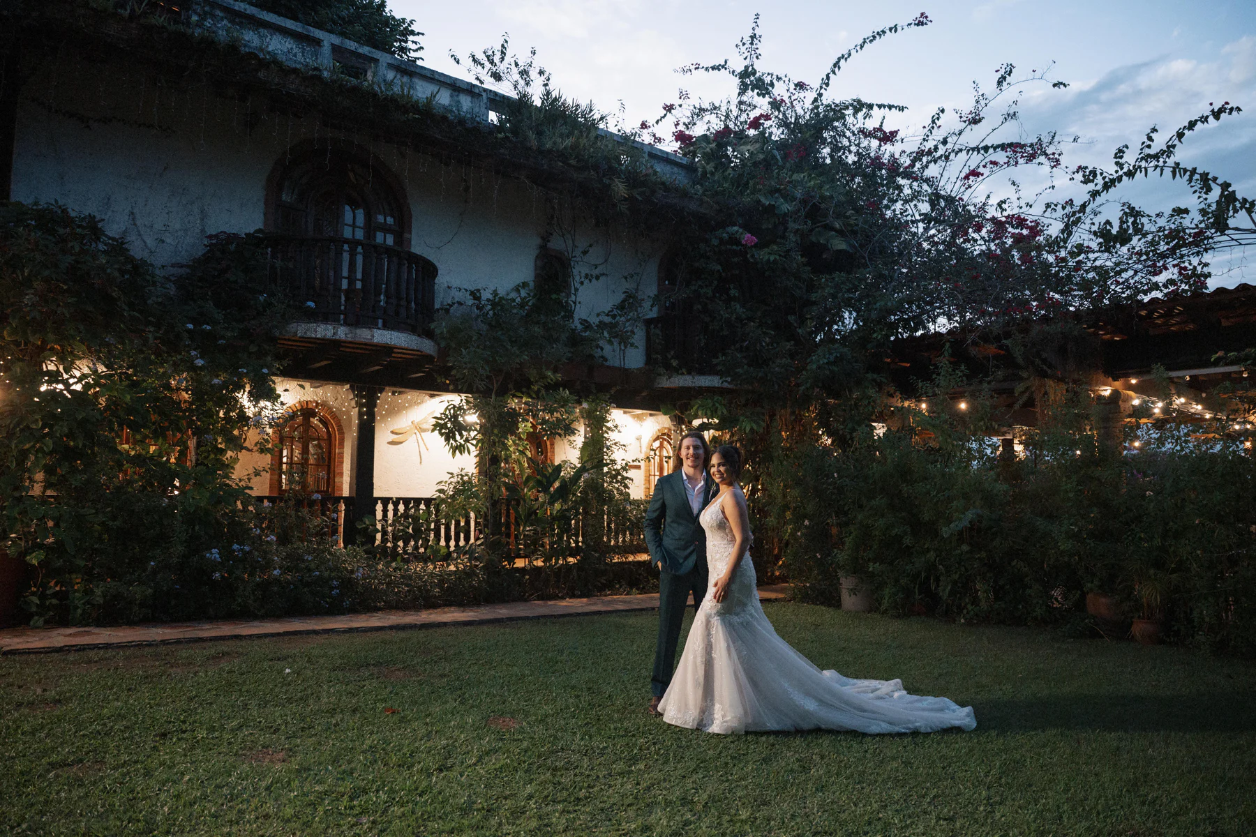 Abigail and Cody on the front lawn at dusk, with the vine-covered hacienda behind them
