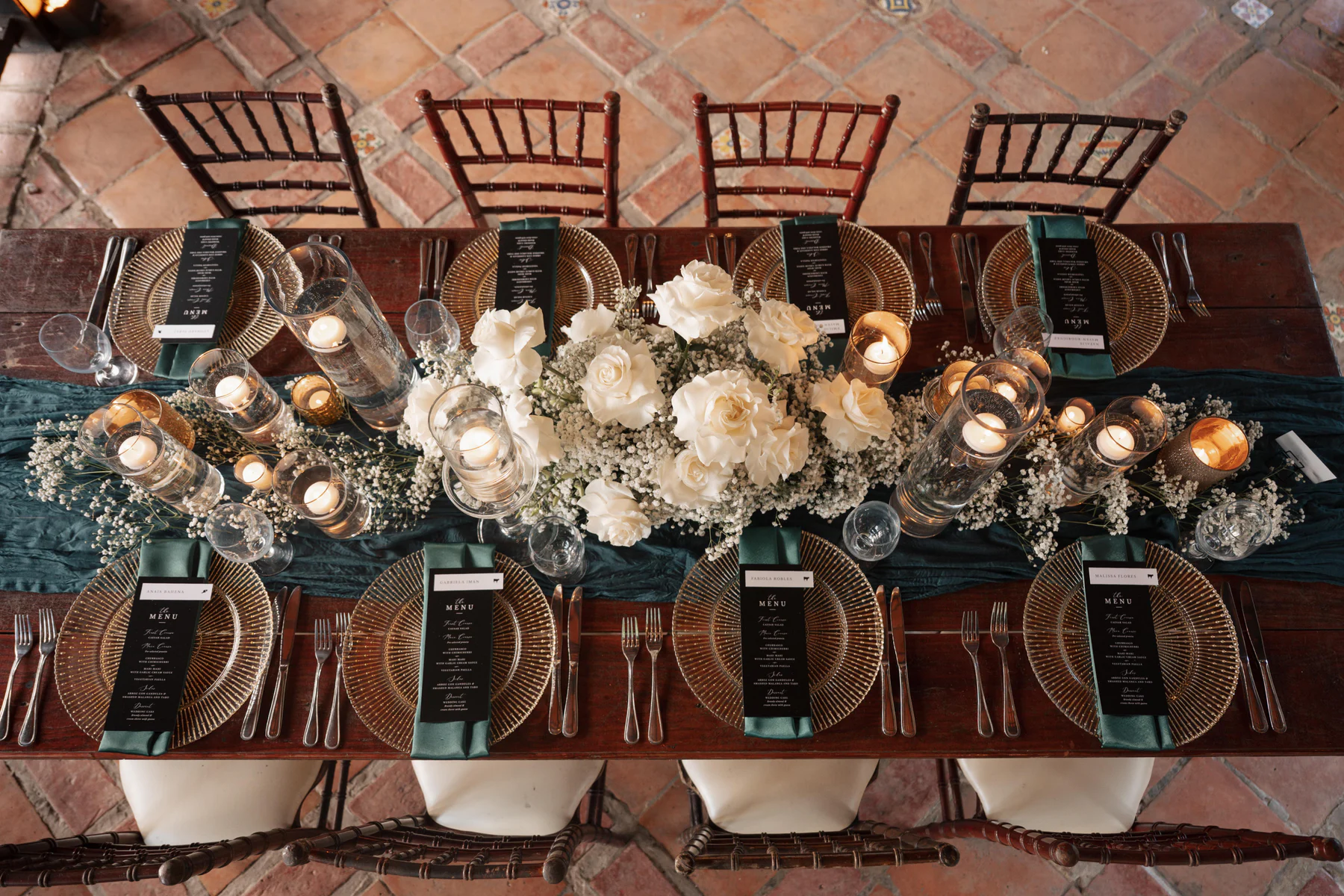 A reception table at Hacienda Siesta Alegre set with white roses, candles, and gold chargers