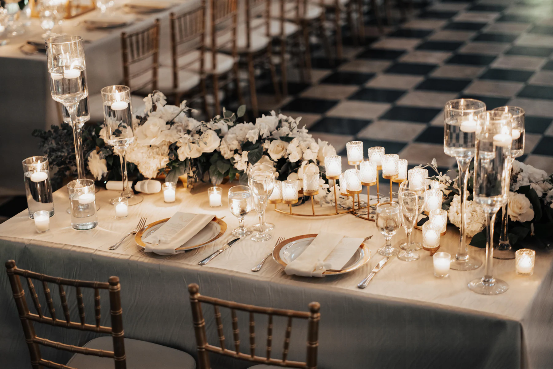 A candlelit reception table with white roses on the checkered floor of the Hotel El Convento ballroom