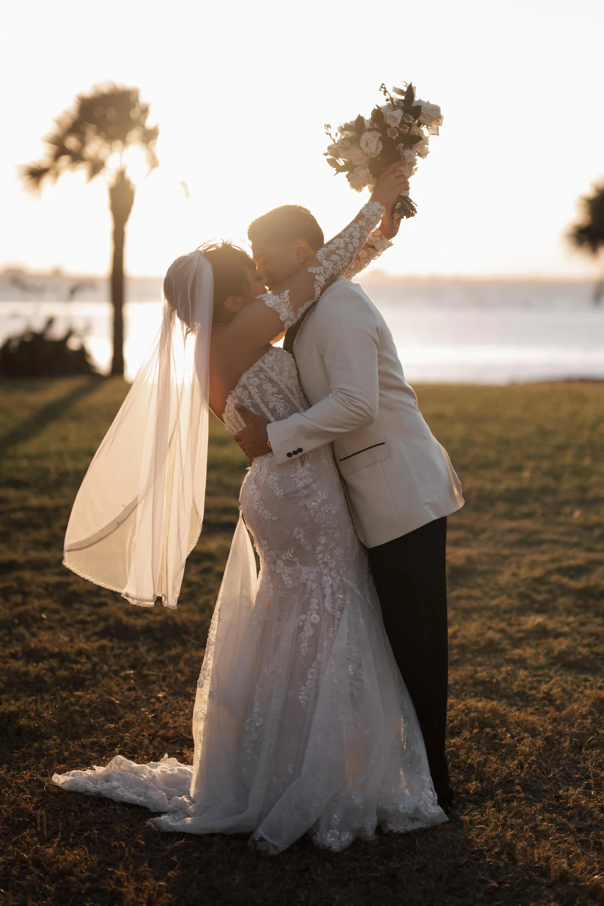Amanda and Sebastian kissing on the lawn at sunset at their Powel Crosley Estate wedding in Sarasota, with Sarasota Bay and a palm tree behind them