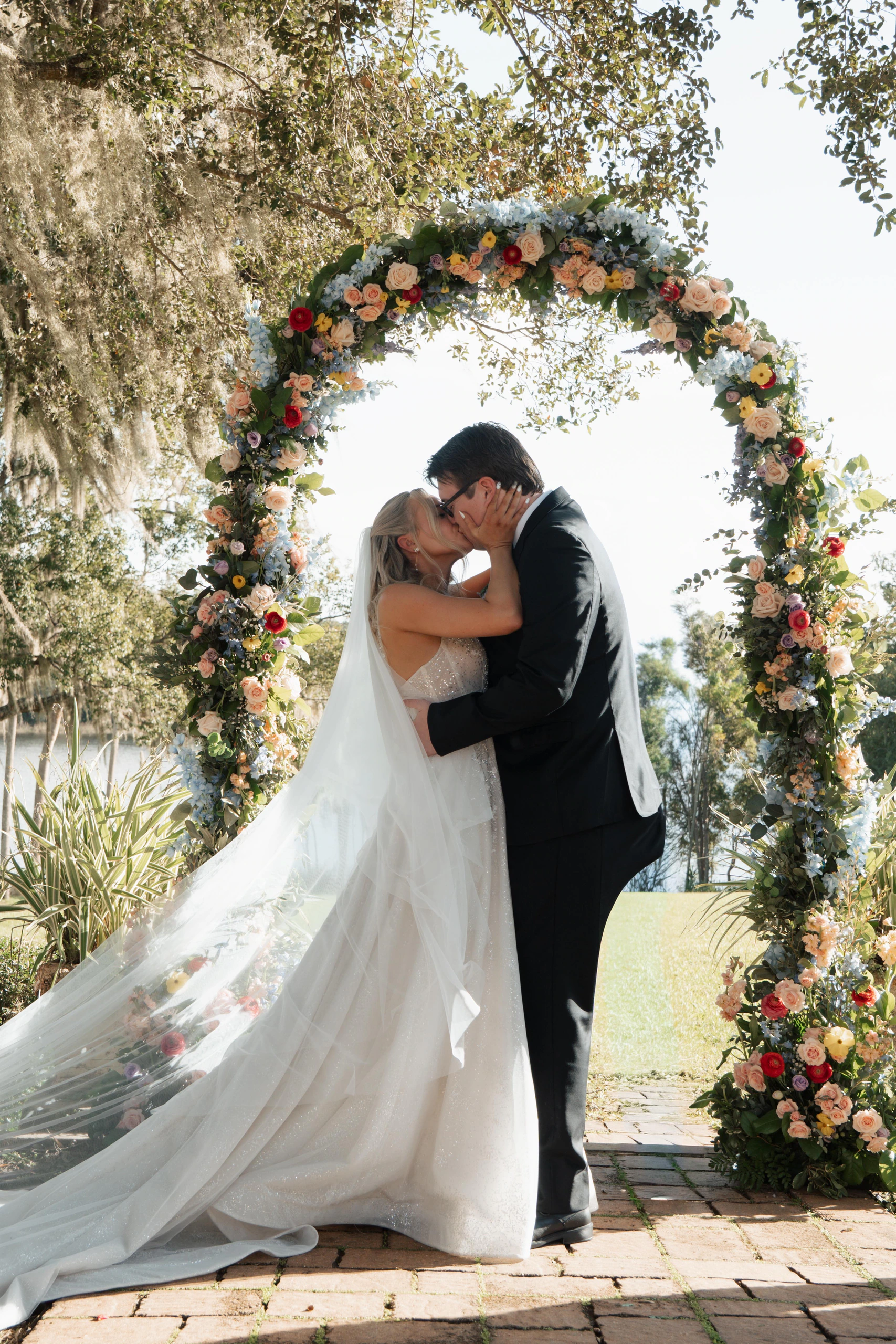 Veronica and Cole sharing their first kiss beneath a floral arch at their Sydonie Mansion wedding in Mount Dora, Florida