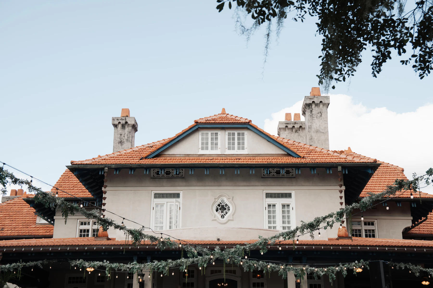 The front of Sydonie Mansion in Mount Dora, with red tile roofs, stone chimneys, and greenery strung with lights