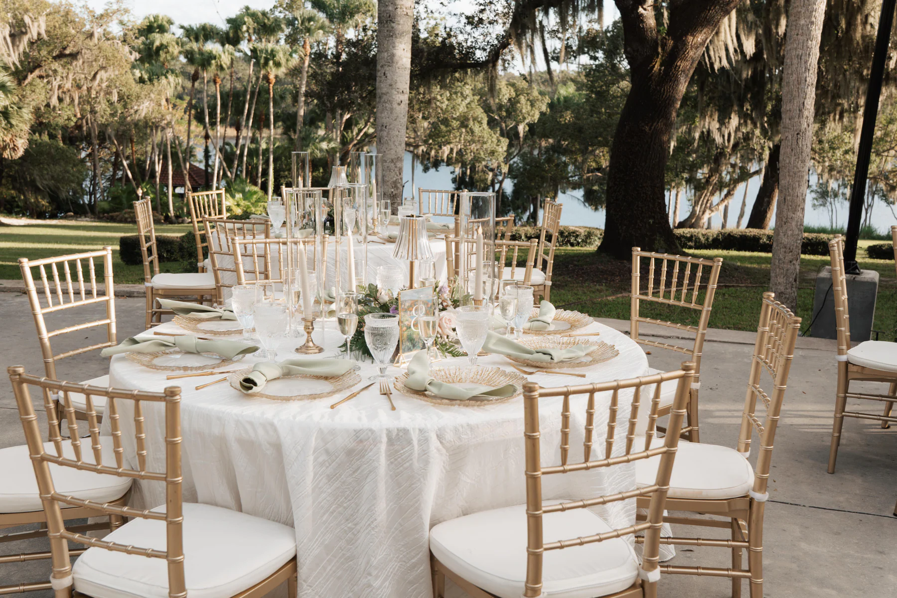 Reception tables with gold chairs set on the terrace at Sydonie Mansion, with the lake and moss draped oaks behind