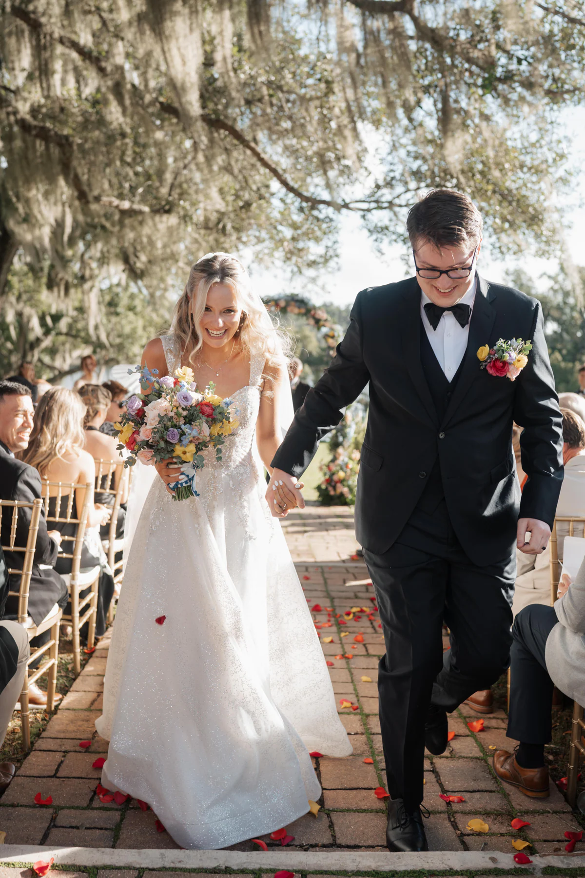 Veronica and Cole walking back down the brick aisle hand in hand after their Sydonie Mansion ceremony, guests cheering on both sides